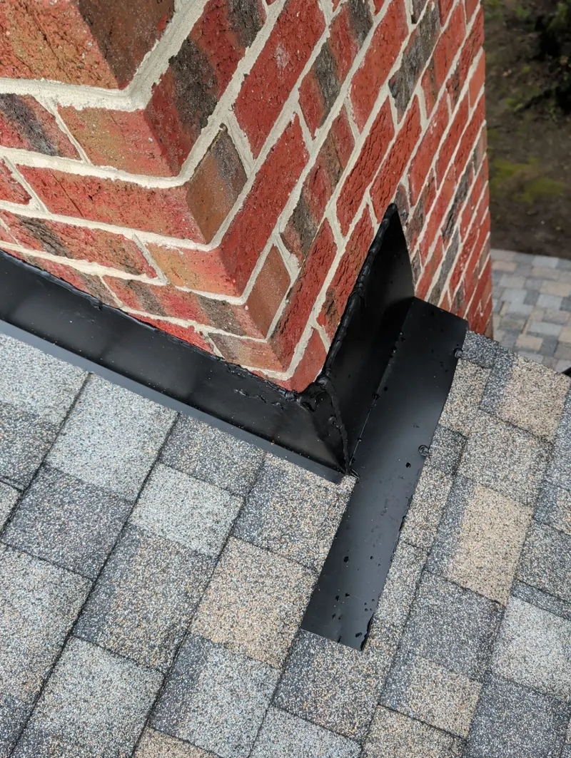 Black flashing where a brick chimney meets new shingles