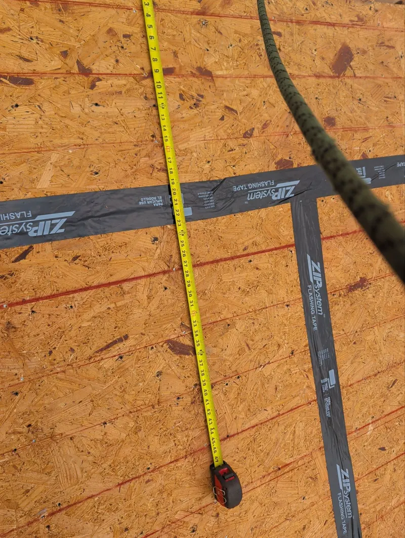 Close-up of black flashing tape sealing a roof deck seam, with a tape measure