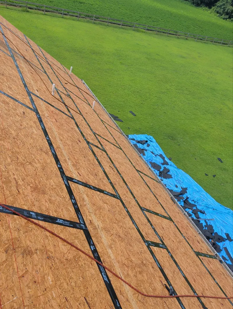 Taped seams across a roof deck slope with a green field beyond