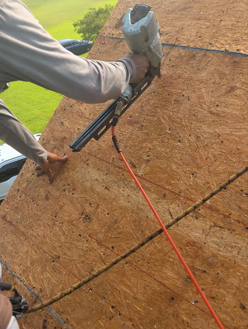 A roofer’s hand and nail gun fastening a roof deck panel