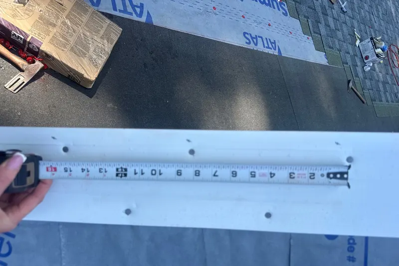 White drip edge with fastener holes beside a tape measure over synthetic underlayment