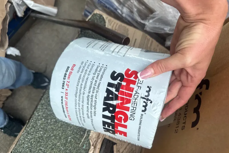 A hand holding a roll of self-adhering shingle starter strip
