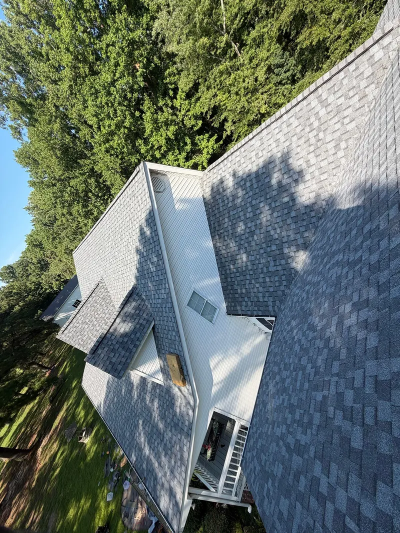 Aerial view of a finished gray shingle roof ridge and hips beside tall trees
