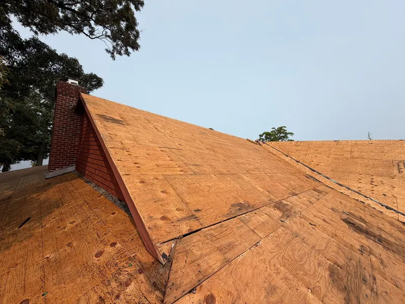 Bare plywood roof deck with the old shingles removed, around a brick chimney