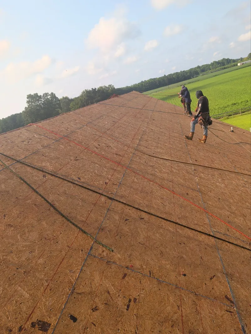 Two roofers working on a bare roof deck marked with chalk lines